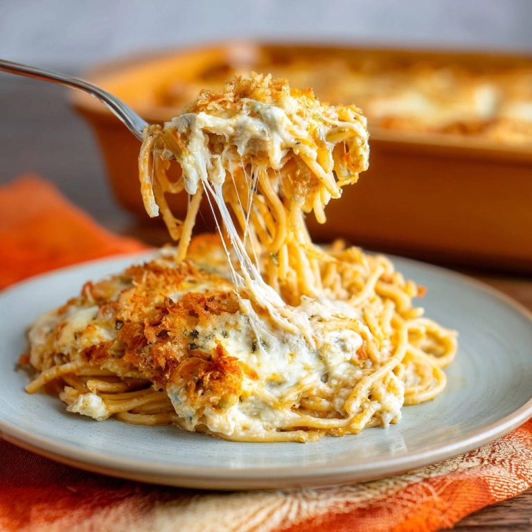 Creamy baked spaghetti bake served on a plate, with a fork lifting cheesy strands in a mesmerizing cheese pull.