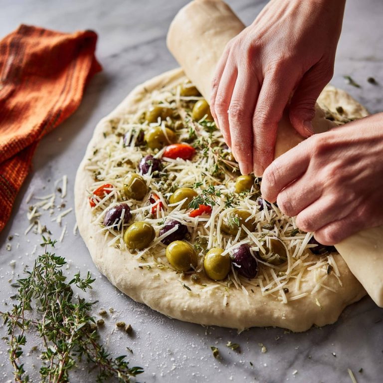 Savory Olive & Herb Rolled Bread preparation step showing hands rolling dough over toppings.