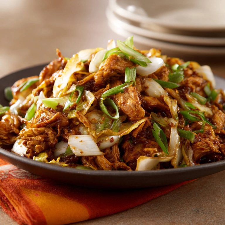 Shredded chicken and cabbage stir-fry served in a dark bowl, garnished with sliced green onions.