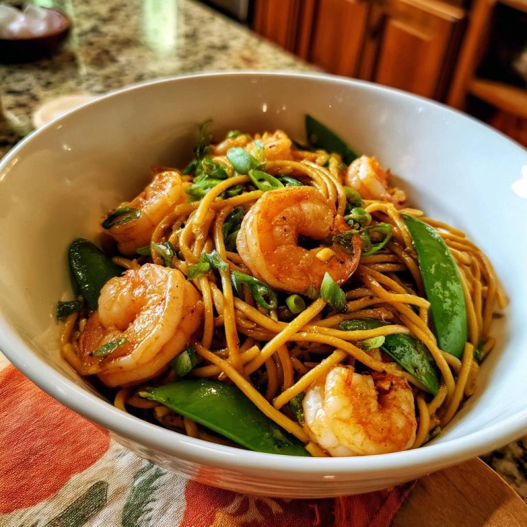 Garlic shrimp noodle stir-fry served in a white bowl with snap peas and green onions.