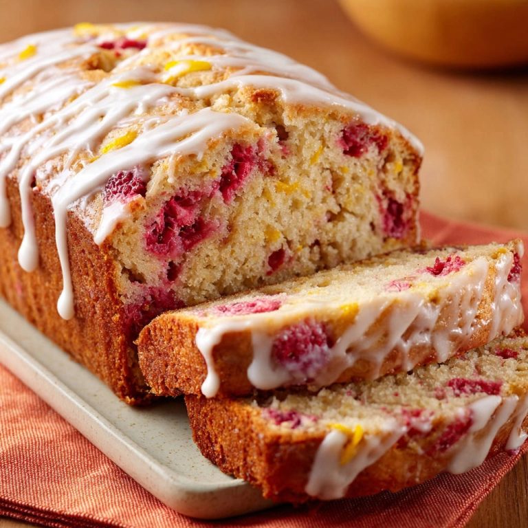 Lemon raspberry quick bread sliced and drizzled with glaze, showing a close-up of the fruit-filled interior.