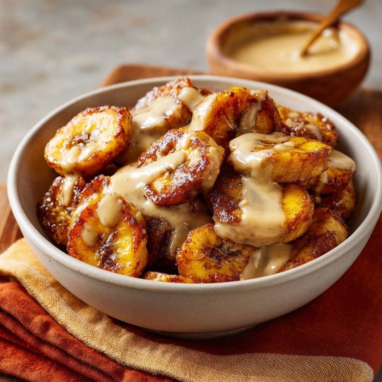 Pan-fried sweet plantains with cream sauce served in a bowl, shown in a close-up view with sauce drizzled over the top.