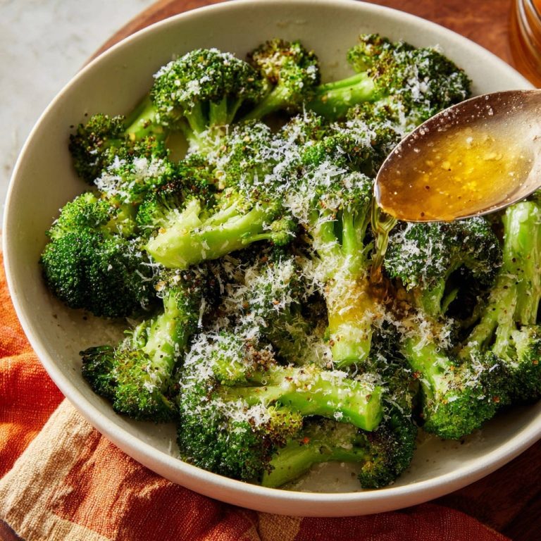Perfect roasted broccoli being drizzled with a golden dressing from a spoon in a white bowl.