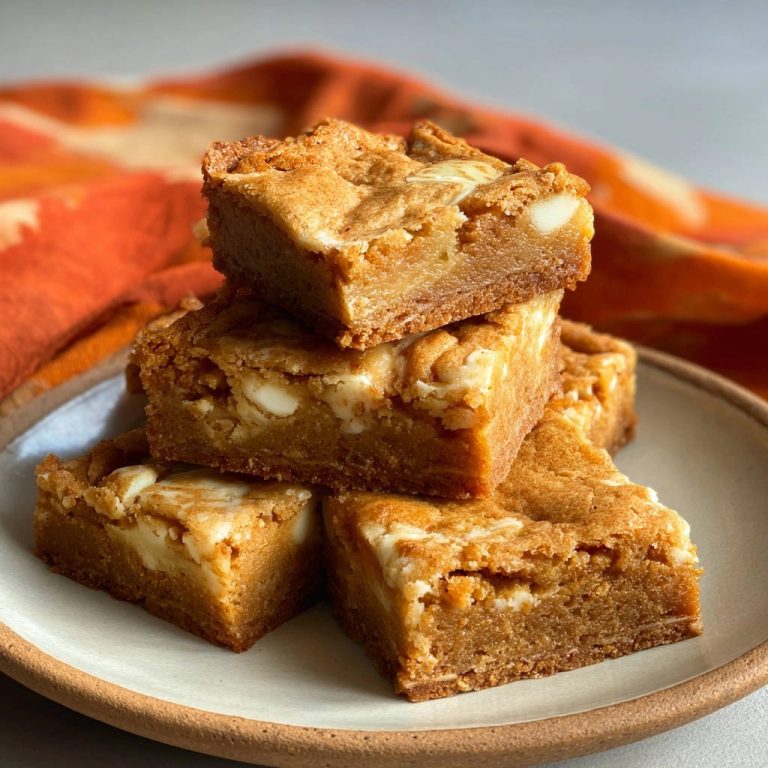 White chocolate chip blondies are stacked in a close-up view on a plate, showcasing their chewy texture.