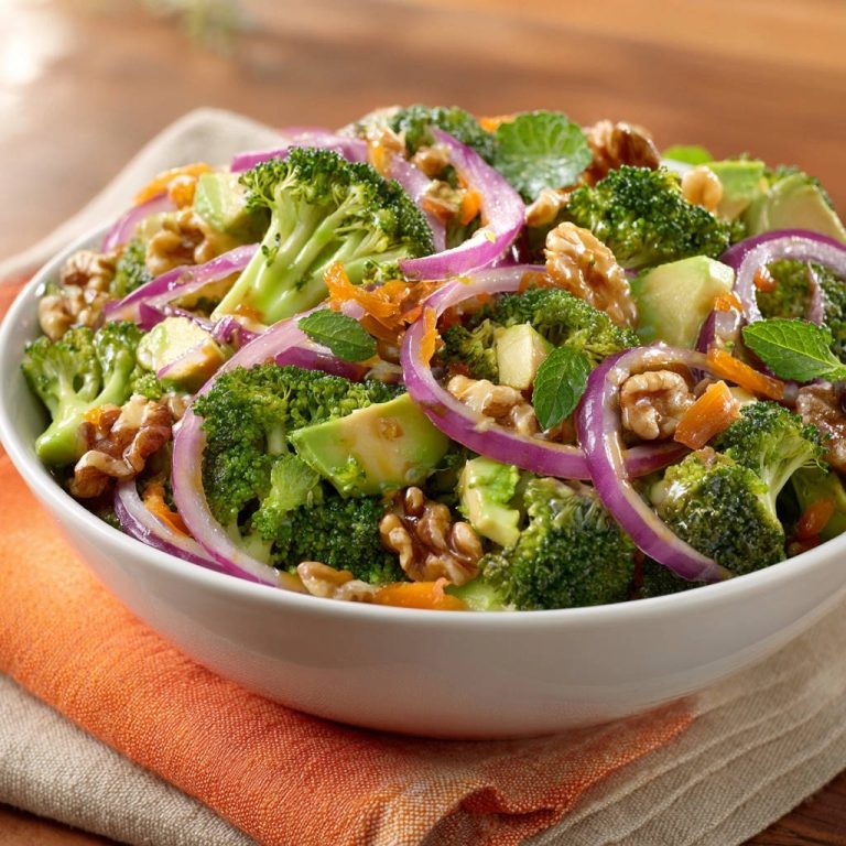 Crunchy broccoli & avocado salad with red onion and walnuts shown in a white bowl with a close-up view.