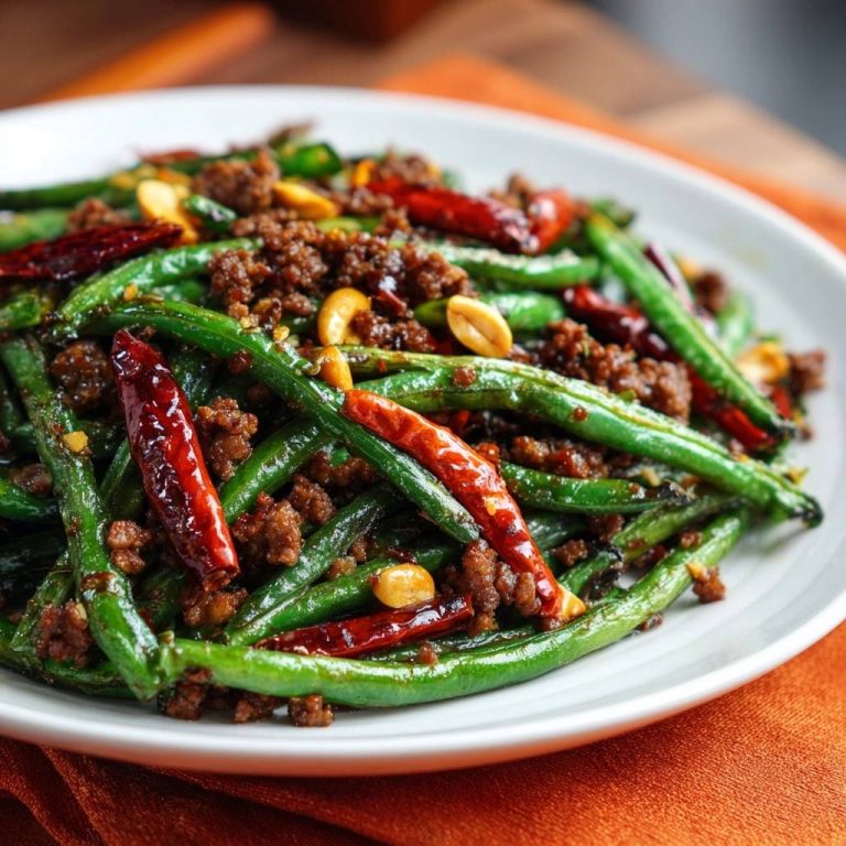 Blistered beef green beans stir-fry served on a white plate, showcasing the glossy texture and spicy chili peppers.