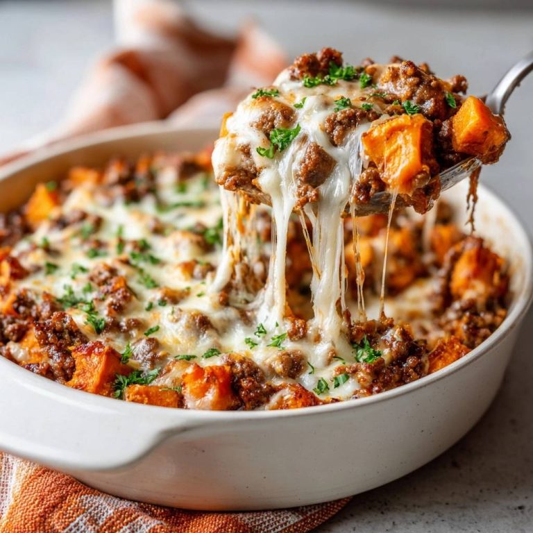 Cheesy beef sweet potato casserole with a gooey cheese pull being lifted by a spoon, garnished with parsley.