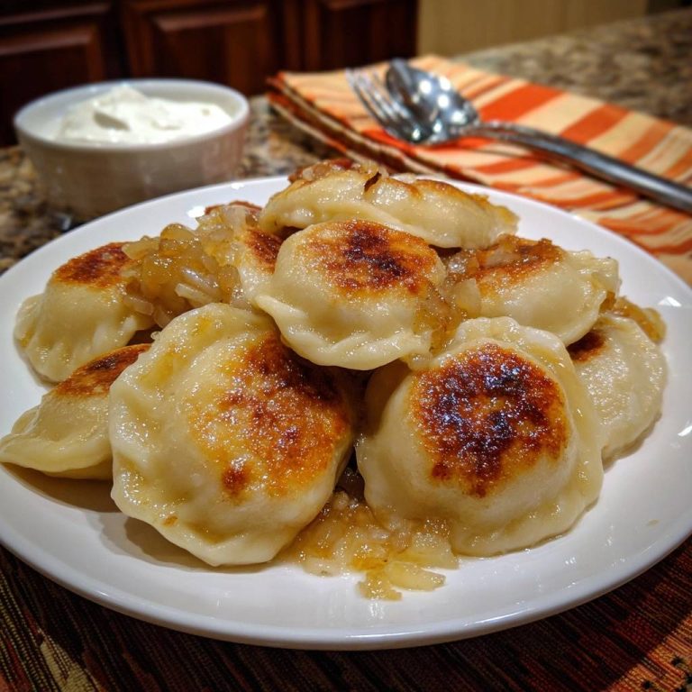 Crispy pierogi with caramelized onions plated on a white dish, showcasing their golden-brown tops and glistening onions.