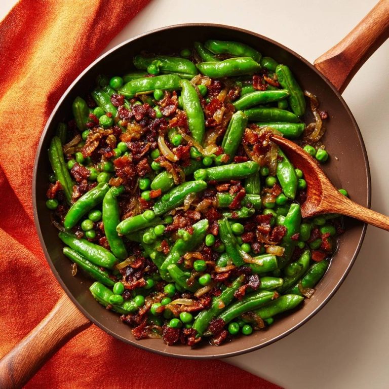 Skillet sugar snap peas with bacon, peas & onions shown in an overhead view in a rustic pan.
