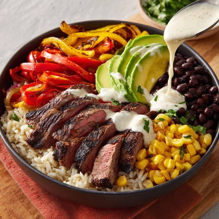Steak fajita power bowl with sliced steak, peppers, avocado, beans, corn, and a creamy sauce being drizzled on top.