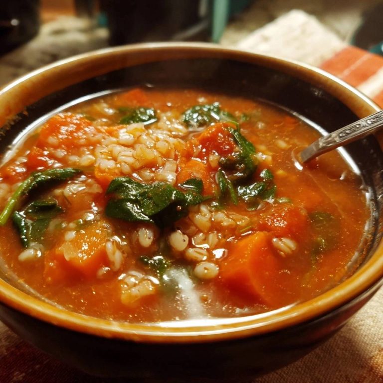 Hearty tomato carrot barley soup close-up showing the texture of the barley, carrots, and spinach in a bowl.