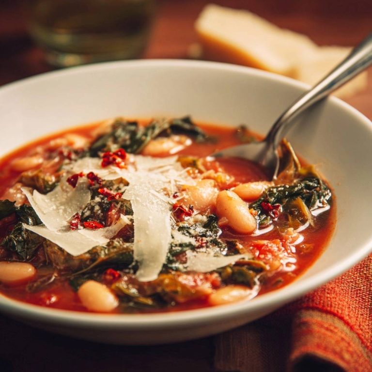 Hearty white bean & greens soup in a bowl, showing a close-up of shaved parmesan and red pepper flake garnish.