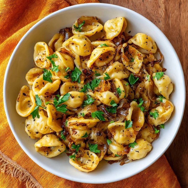 Cheesy tortellini with caramelized onions in a white bowl, viewed from directly above and garnished with fresh parsley.