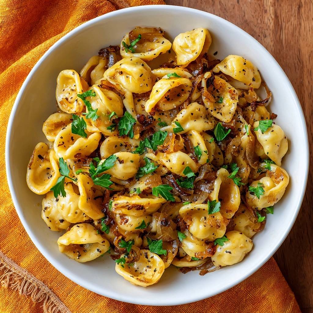Cheesy tortellini with caramelized onions in a white bowl, viewed from directly above and garnished with fresh parsley.