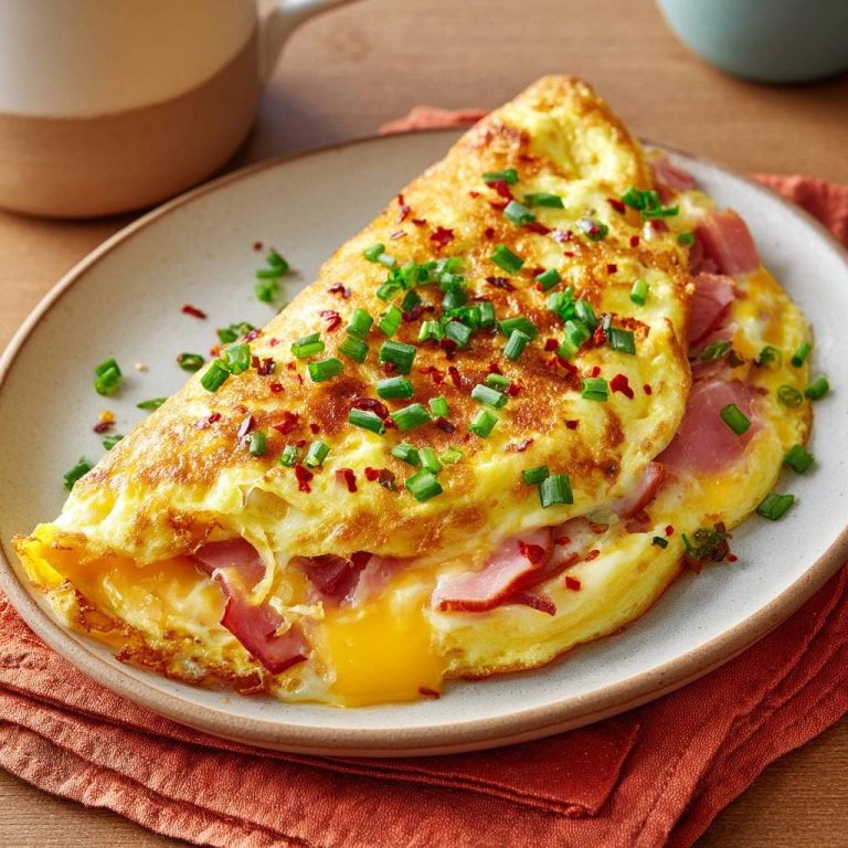 Ham and cheese omelette with a gooey center and fresh chive garnish, sliced to show the interior.