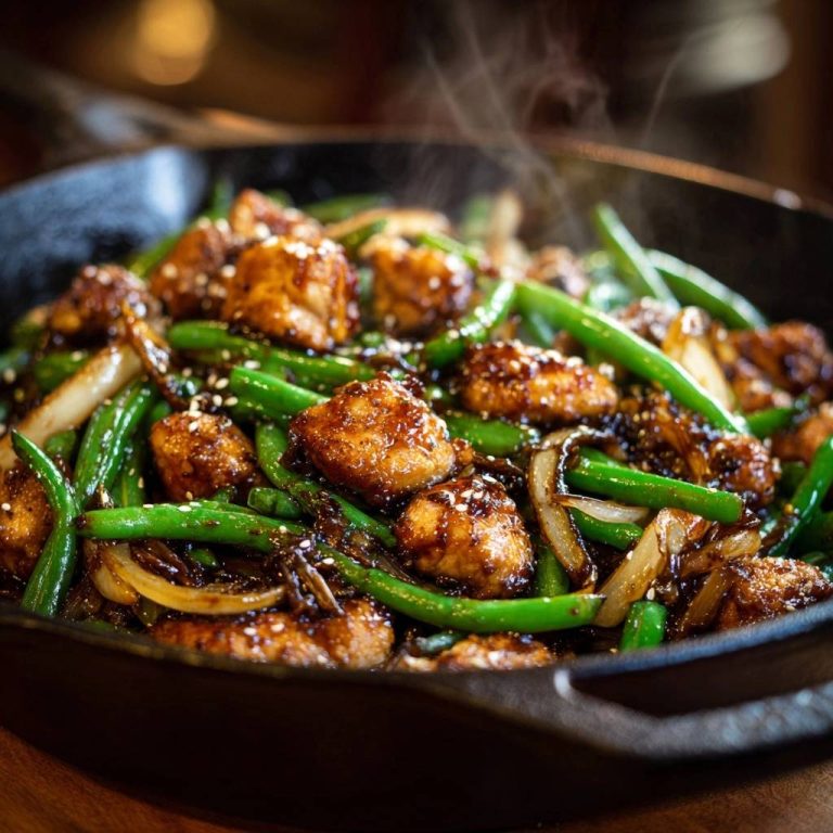 Crispy chicken green bean stir-fry steaming in a cast-iron skillet, garnished with sesame seeds.