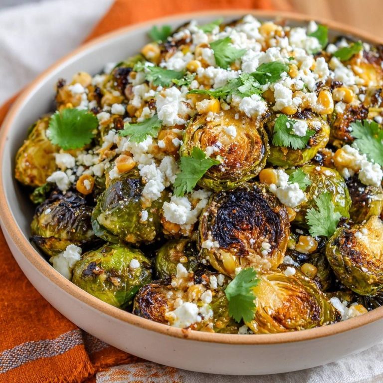 Elote-style roasted Brussels sprouts topped with crumbled cheese, corn, and cilantro in a bowl.