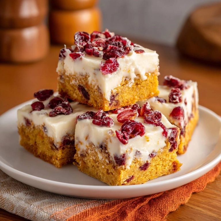 Pumpkin cranberry bars with light fluffy texture stacked on a white plate and garnished with dried cranberries.