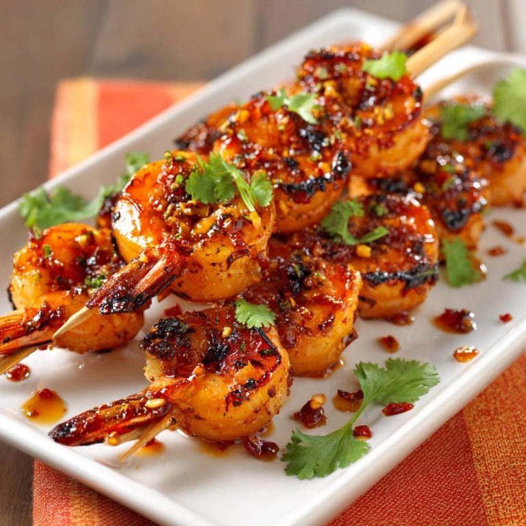 Sticky chili garlic shrimp skewers are presented on a white platter, showcasing a close-up view of the glazed shrimp on wooden skewers.
