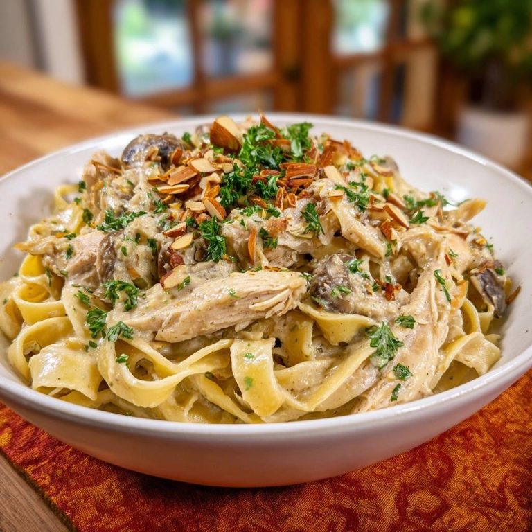 Creamy chicken mushroom fettuccine with thick sauce, generously garnished with toasted almonds and fresh parsley.