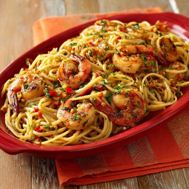Garlic butter shrimp linguine served in a red platter, showcasing grilled shrimp and a fresh herb garnish.