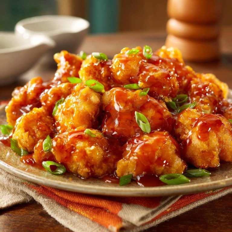 Crispy General Tso's Chicken generously glazed and garnished with sliced green onions on a plate.