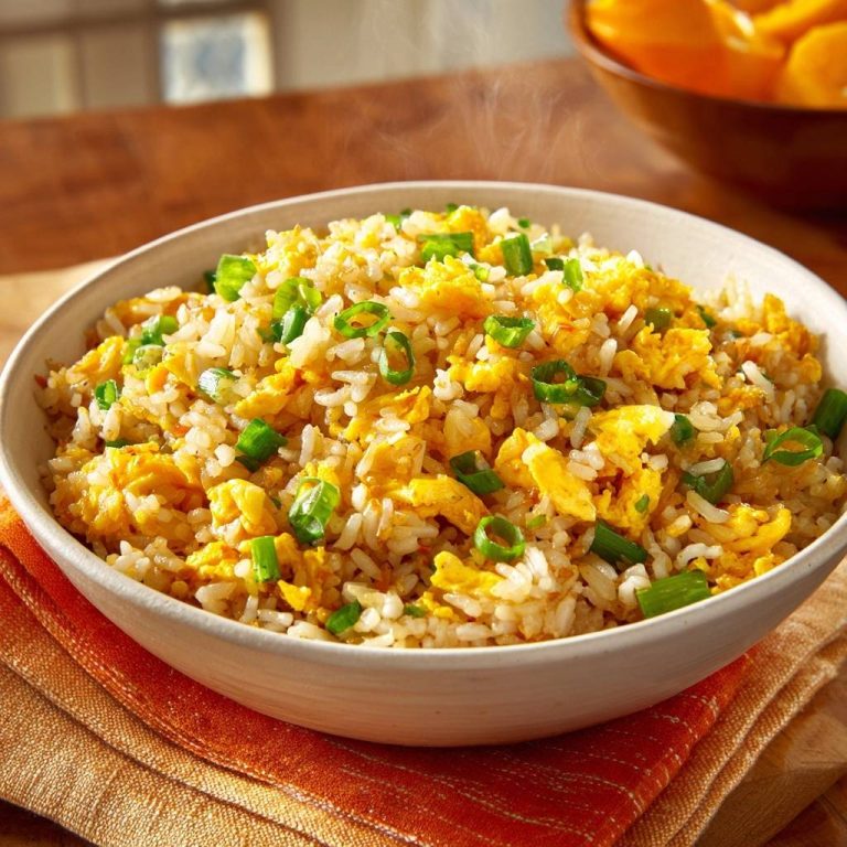 Golden egg fried rice served in a steaming white bowl, close-up view showing fluffy grains and green onions.