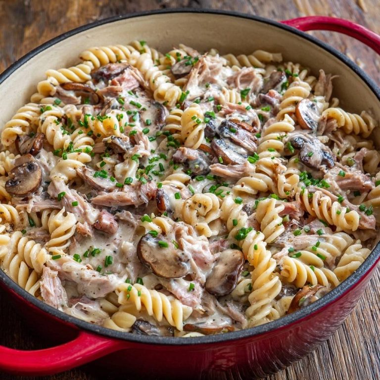 Creamy mushroom and shredded chicken rotini served in a red dutch oven, garnished with fresh chives.